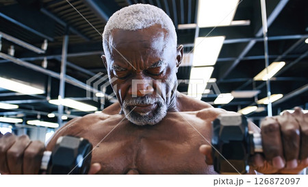Senior african american athlete lifting weights, concentrating on his workout in a modern gym, demonstrating strength and dedication to fitness 126872097