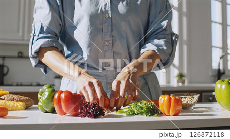 Female hands seasoning vibrant vegan salad with peppers, kale, nuts, lemon, creating fresh culinary composition in contemporary kitchen space 126872118