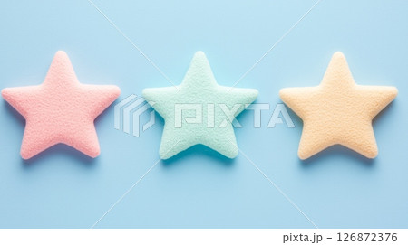 Three Colorful Star-Shaped Sponges on Light Blue Background - Pastel Pink, Green, and Yellow 126872376