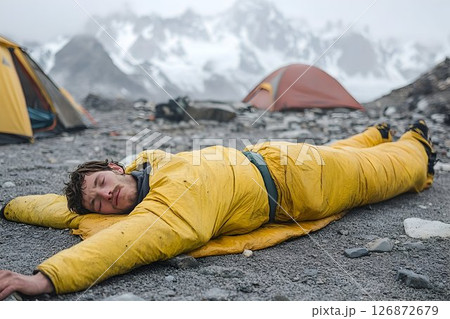Exhausted Climber Rests in Yellow Sleeping Bag near Mountain Cam 126872679