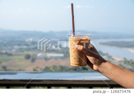 Cropped shot view of someone hand holding a plastic cup of iced milk coffee. 126873476