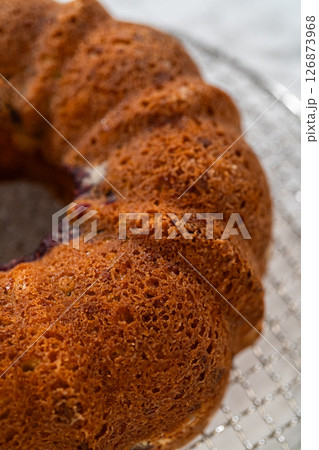 With precision, the bundt cake is carefully removed from the pan - placed onto a round cooling rack, preparing it for a flawless presentation and delightful indulgence. 126873968
