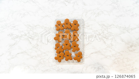 Flat lay close-up showing neatly arranged gingerbread man cookies cooling on a wire rack, showcasing their golden-brown tones and festive shapes. Flat lay close-up showing neatly arranged gingerbread man cookies cooling on a wire rack, showcasing their golden-brown tones and festive shapes. 126874065