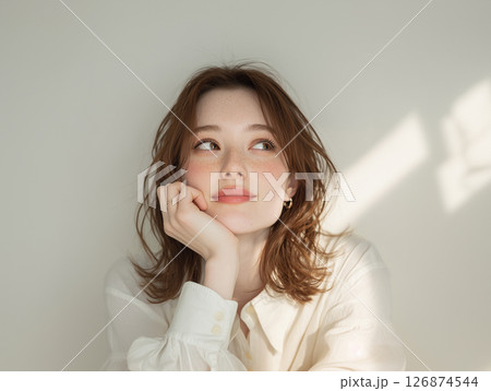 白い服と自然光が印象的な頬杖をつく女性のポートレート 126874544