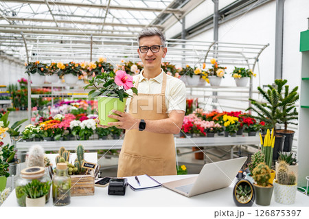 A Caucasian male florist stands in a shop holding a potted plant for sale. A Caucasian male florist stands in a shop holding a potted plant for sale. 126875397