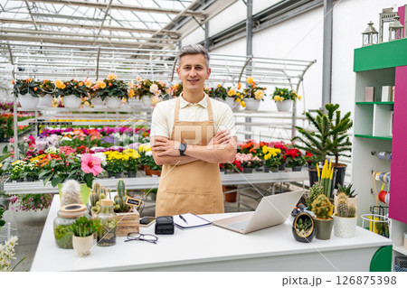 A Caucasian man in a florist shop, standing behind the table with various plants, smiling at the camera. A Caucasian man in a florist shop, standing behind the table with various plants, smiling at the camera. 126875398