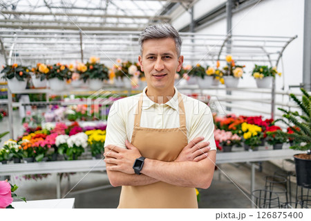 A Caucasian man, arms crossed, in his flower shop. He is surrounded by an array of flowers and potted plants on display for sale. A Caucasian man, arms crossed, in his flower shop. He is surrounded by an array of flowers and potted plants on display for sale. 126875400