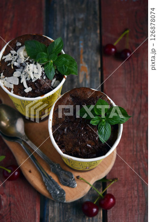 Pair of chocolate desserts with coconut topping and mint leaves in yellow cups on rustic wooden table ideal for dessert menu photography cozy food styling and bakery promotions Pair of chocolate desserts with coconut topping and mint leaves in yellow cups on rustic wooden table ideal for dessert menu photography cozy food styling and bakery promotions 126878074