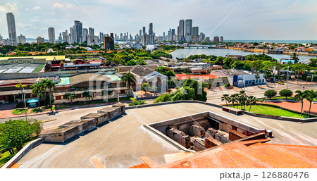 View of modern high-rises and waterfront neighborhoods in Cartagena, Colombia seen from the elevated platform of Castillo San Felipe de Barajas. The photo contrasts colonial stone structures in the 126880476