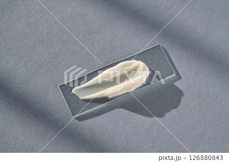 The texture of white cream on a slide on a blue background. The texture of white cream on a slide on a blue background. 126880843