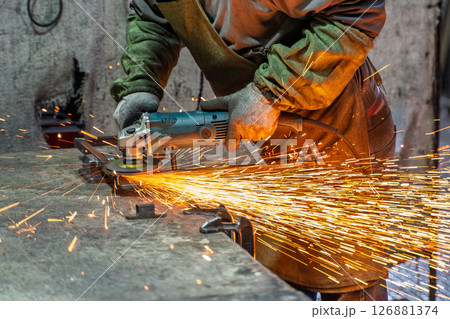 A detailed view of an angle grinder in action as it produces bright sparks while cutting metal in an industrial setting. A detailed view of an angle grinder in action as it produces bright sparks while cutting metal in an industrial setting. 126881374