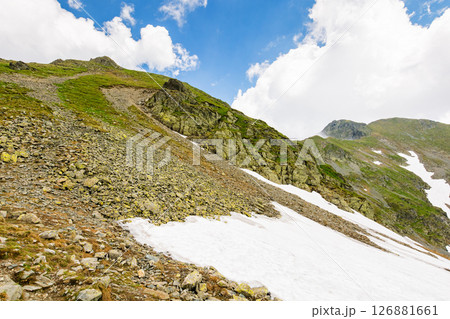 landscape with mountain and blue sky with clouds. snow on the hillside. steep hill with stones and grass. beautiful nature of romania in summer landscape with mountain and blue sky with clouds. snow on the hillside. steep hill with stones and grass. beautiful nature of romania in summer 126881661