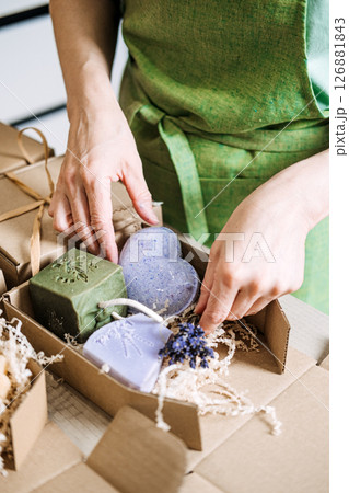 Person arranges handmade soaps with dried lavender into a kraft box for gifting or shipment. Artisanal skincare, small batch soap, eco-friendly packaging, indie beauty brand 126881843