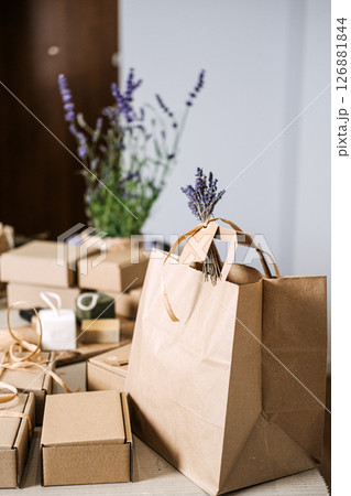 Natural soap gift boxes and kraft bags are arranged on a table with floral decor. Handmade gifts, holiday prep, natural skincare gift, wellness gift box 126881844