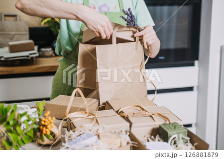 Person wraps natural soaps in kraft packaging for a small business in a home kitchen. Handmade product packaging, creative process, DIY business visuals, home-based business Person wraps natural soaps in kraft packaging for a small business in a home kitchen. Handmade product packaging, creative process, DIY business visuals, home-based business 126881879