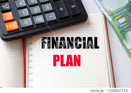 FINANCIAL PLAN word inscription in a notebook, calculator and a pile of money. FINANCIAL PLAN word inscription in a notebook, calculator and a pile of money. 126882258