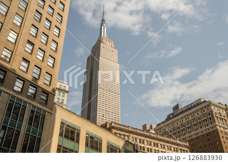 The iconic Empire State Building towers above surrounding structures. The photo captures its pointed spire and detailed windows on a clear day. The iconic Empire State Building towers above surrounding structures. The photo captures its pointed spire and detailed windows on a clear day. 126883930