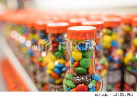 A close-up shot shows a front bottle of colorful candies in sharp focus. More bottles blur into the background in a soft bokeh effect. 126883962