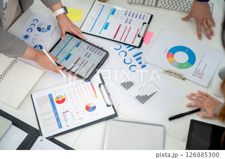 Top view of a working desk with a pair of hand holding a digital tablet and scattered documents. 126885300