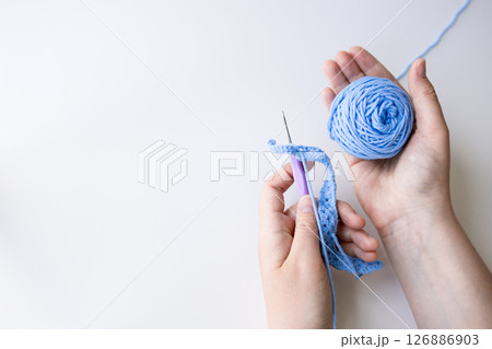 Hands crafting with blue yarn and crochet hook on white background Hands crafting with blue yarn and crochet hook on white background 126886903