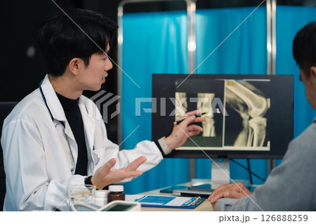 Male doctor explains knee osteoarthritis and arthroplasty treatment after x-ray. Male doctor explains knee osteoarthritis and arthroplasty treatment after x-ray. 126888259