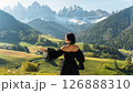 Visit Italy. An attractive young woman in a black, elegant dress, surrounded by sunny fields and high mountains in nature at sunrise. Travel incentive to the Dolomites 126888310