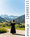 Visit Italy. Early sun spills over a woman in an elegant black dress, lost in the vastness of alpine fields and mountain silence, a serene call to the Dolomites 126888315