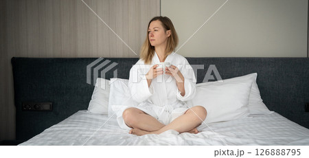 Woman in white bathrobe lying on sofa and relaxing with cup of tea at home. 126888795