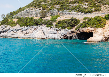 Sea cave in a rocky shore with turquoise transparent water. Picturesque natural landscape with rough texture of stones and deep entrance to the grotto. Ecotourism. Fascinating seascape. Sea cave in a rocky shore with turquoise transparent water. Picturesque natural landscape with rough texture of stones and deep entrance to the grotto. Ecotourism. Fascinating seascape. 126889677