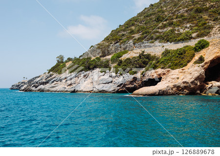 Sea cave in a rocky shore with turquoise transparent water. Picturesque natural landscape with rough texture of stones and deep entrance to the grotto. Ecotourism. Fascinating seascape. Sea cave in a rocky shore with turquoise transparent water. Picturesque natural landscape with rough texture of stones and deep entrance to the grotto. Ecotourism. Fascinating seascape. 126889678