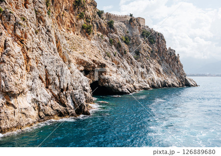 Sea cave in a rocky shore with turquoise transparent water. Picturesque natural landscape with rough texture of stones and deep entrance to the grotto. Ecotourism. Fascinating seascape. 126889680