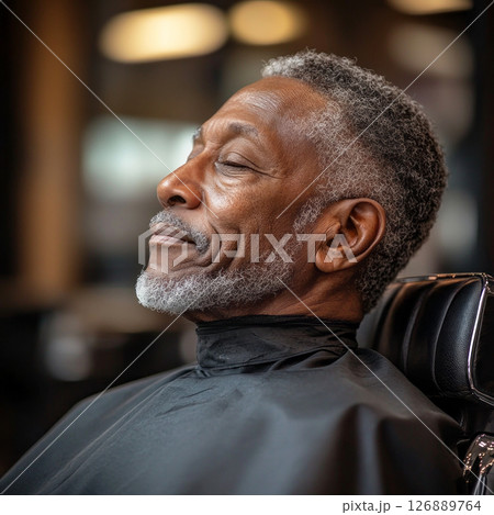 An elderly African American man relaxes in a barber chair while receiving a haircut at a local barber shop. The atmosphere is inviting and lively, showcasing community engagement 126889764