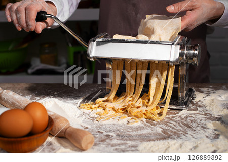 Caucasian female hands making fettuccine noodles using mechanical pasta machine Caucasian female hands making fettuccine noodles using mechanical pasta machine 126889892