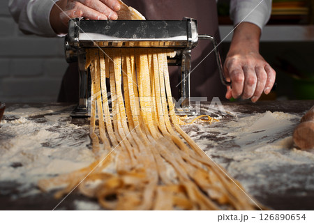 Caucasian female hands making fettuccine noodles using mechanical pasta machine Caucasian female hands making fettuccine noodles using mechanical pasta machine 126890654
