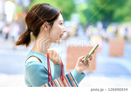 ショッピングしながらスマホを操作するオシャレな若い女性 ショッピングしながらスマホを操作するオシャレな若い女性 126890834