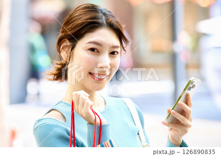 ショッピングしながらスマホを操作するオシャレな若い女性 ショッピングしながらスマホを操作するオシャレな若い女性 126890835