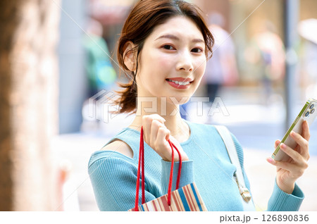 ショッピングしながらスマホを操作するオシャレな若い女性 ショッピングしながらスマホを操作するオシャレな若い女性 126890836
