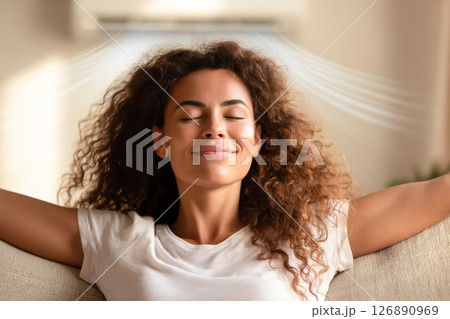 Air Conditioning Appreciation Day. Woman relaxing on a sofa enjoying cool air from an air conditioning unit, celebrating Air Conditioning Appreciation Day 126890969