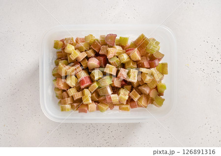Freshly chopped frozen rhubarb prepared in plastic box on white background. Trendy organic food. View from above. 126891316