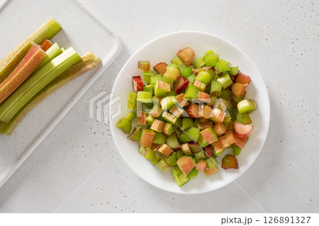 Freshly chopped rhubarb in white plate on white background. Trendy organic food. Ready for cooking. Vegan concept. View from above. Freshly chopped rhubarb in white plate on white background. Trendy organic food. Ready for cooking. Vegan concept. View from above. 126891327