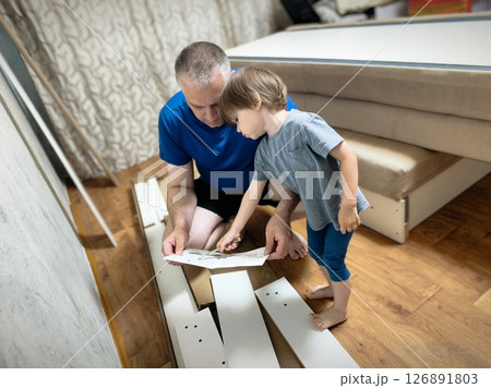 Father and son assembling furniture. Boy helping his dad at home. Happy Family concept. Dad and son assemble furniture together Father and son assembling furniture. Boy helping his dad at home. Happy Family concept. Dad and son assemble furniture together 126891803