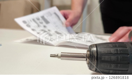 cordless screwdriver or screwdriver. Furniture assembly process. man reads the instructions for assembling furniture cordless screwdriver or screwdriver. Furniture assembly process. man reads the instructions for assembling furniture 126891818