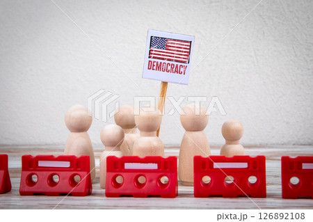 Wooden Figures Holding Democracy Sign with Red Barriers Representing Protest or Political Action 126892108