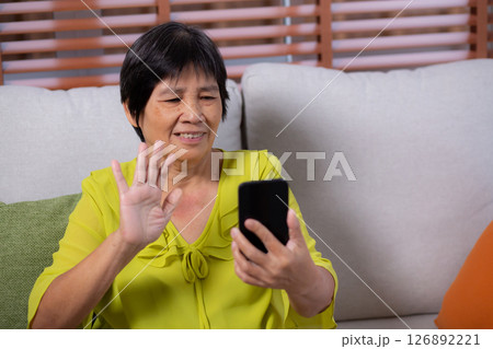 Senior asian woman sitting on sofa looking smartphone for video call in living room. Senior asian woman sitting on sofa looking smartphone for video call in living room. 126892221