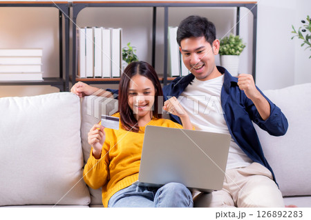 Happy asian couple using laptop and credit card for online shopping together in living room. Happy asian couple using laptop and credit card for online shopping together in living room. 126892283