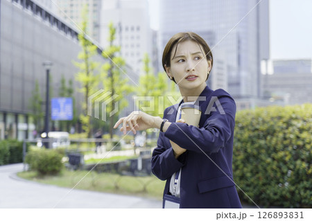 オフィス街で紙コップを手に時間を気にする若いビジネスウーマン 126893831
