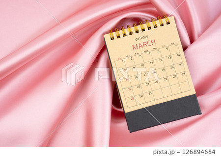 March 2026 craft brown paper desk calendar on pink silk textile background. March 2026 craft brown paper desk calendar on pink silk textile background. 126894684