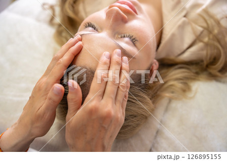 Hands of a female practitioner positioned on the face of a young woman during an Access Bars facial lifting session. Concept of energy work, healing touch and alternative face therapy Hands of a female practitioner positioned on the face of a young woman during an Access Bars facial lifting session. Concept of energy work, healing touch and alternative face therapy 126895155