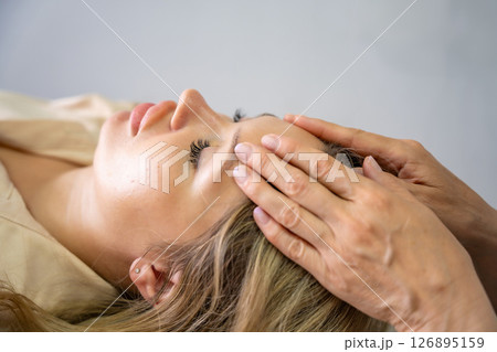 Hands of a female practitioner positioned on the face of a young woman during an Access Bars facial lifting session. Concept of energy work, healing touch and alternative face therapy Hands of a female practitioner positioned on the face of a young woman during an Access Bars facial lifting session. Concept of energy work, healing touch and alternative face therapy 126895159