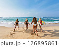 Four women holding surfboards run on tropical beach towards ocean waves. Bikini sport lovers enjoy surfing adventure, explore seaside holiday spot. Friends bond in surf trip, summer travel fun. 126895861